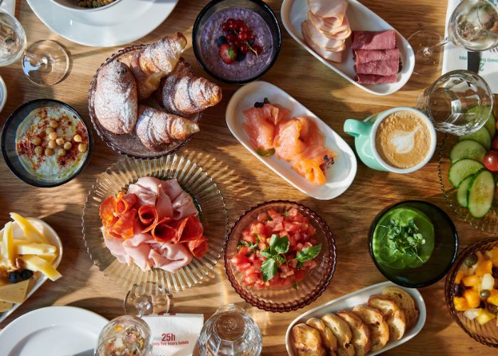 A vibrant brunch spread on a wooden table, featuring croissants, sliced meats, smoked salmon, salads, a cappuccino, and fresh fruit, evoking a cozy and inviting atmosphere.